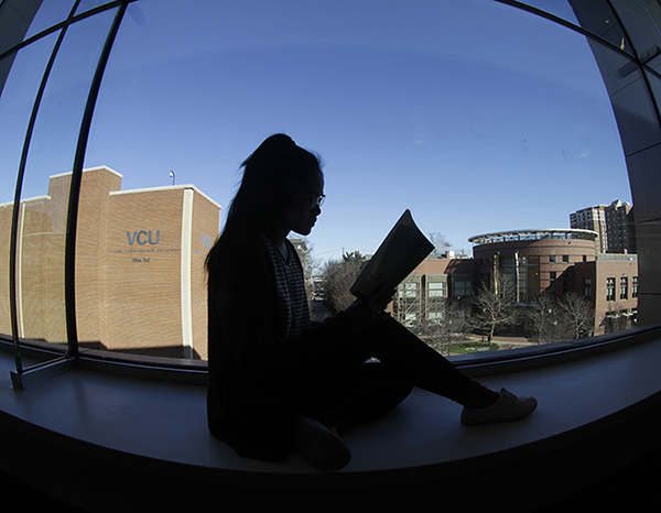 Silhouette of student reading in a window of Cabell library